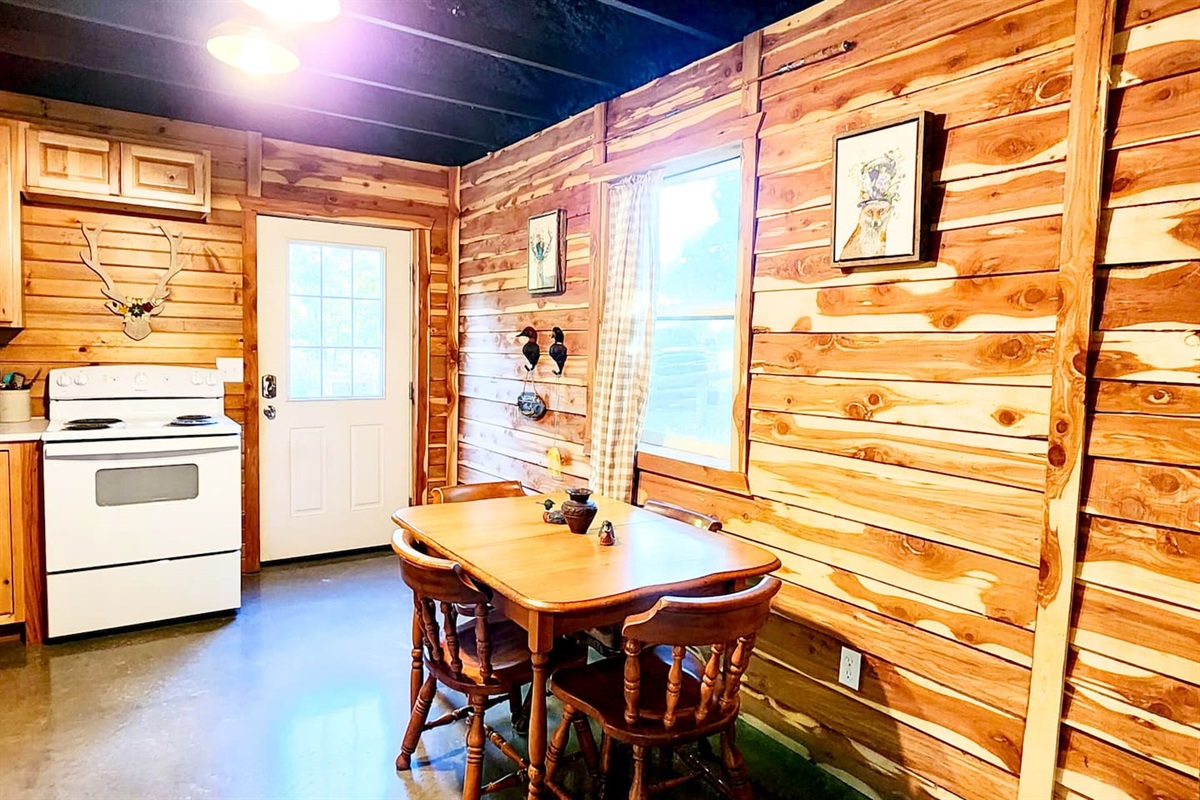 Natural light filters through gingham curtains in this charming dining nook. The wooden table seats four comfortably, just steps from the kitchen—perfect for family meals, card games, or quiet morning coffee in your private lodge escape.