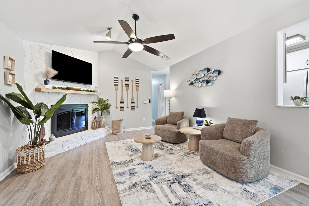 A bright coastal-inspired living room with comfortable seating, a large TV, and a statement fireplace.