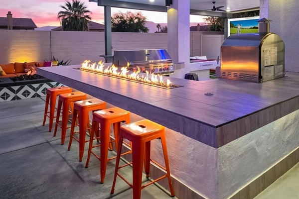 Outdoor kitchen with natural gas BBQ, pizza oven, and tabletop fire feature.
