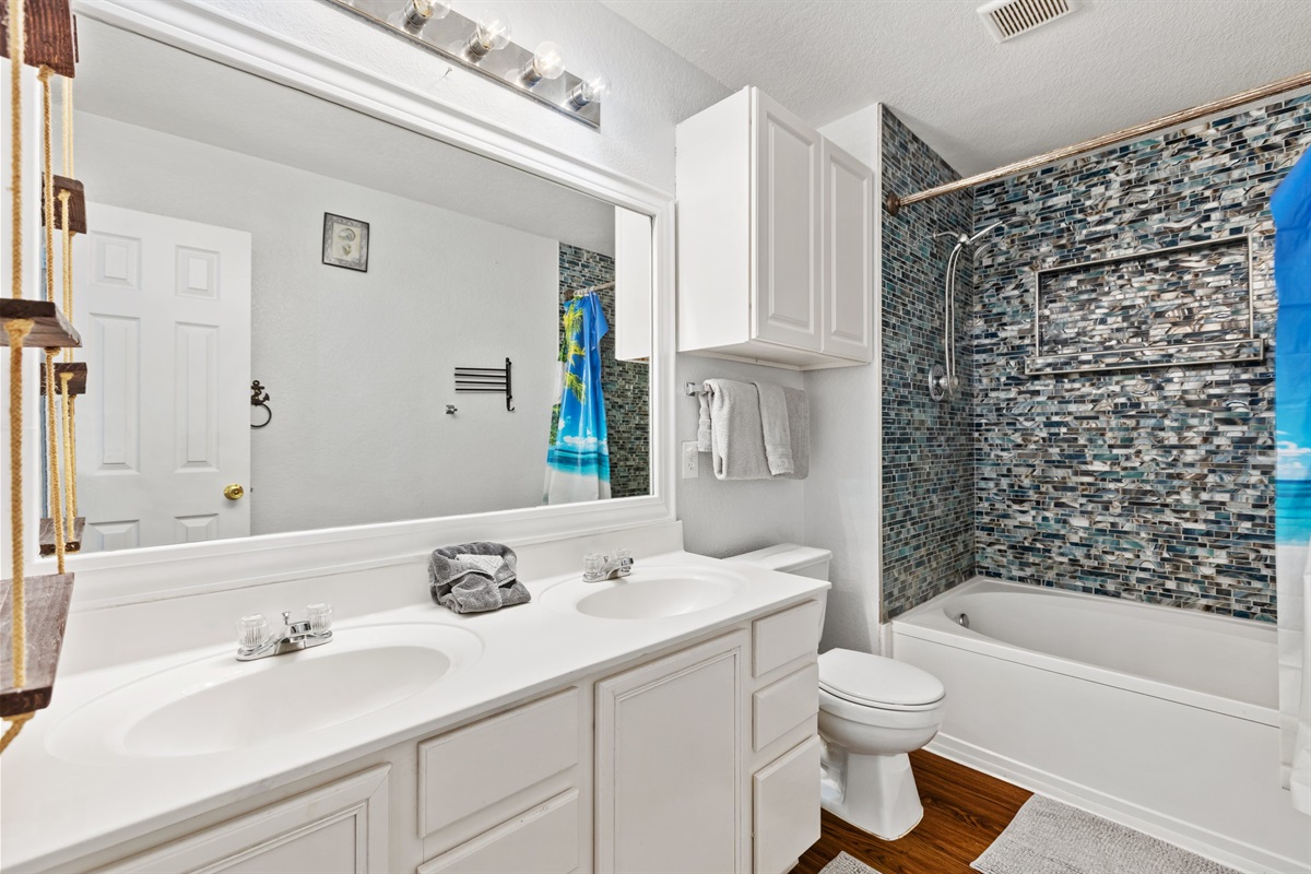 Upstairs bathroom with double sink vanity and stone tile shower and bath tub. Stocked with Ginger Lily Farms toiletries. Fresh towels provided. Built to handle the morning rush for groups of up to 10 guests.