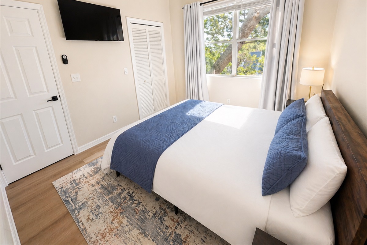 Bright and peaceful bedroom with a comfortable bed, soft linens, and warm wood accents. Large window brings in natural light, while bedside tables and lamps create a cozy, relaxing space for restful nights.