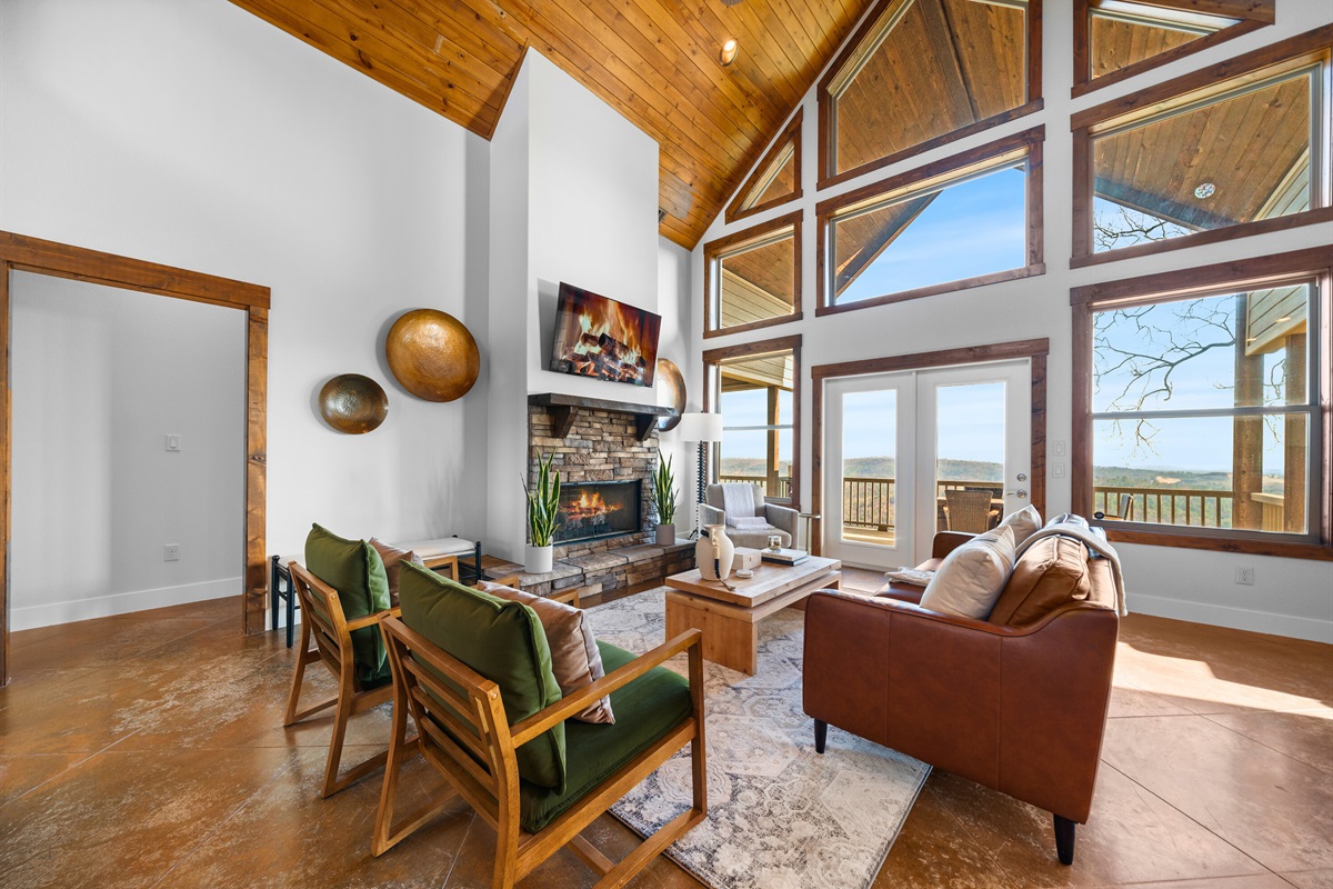 Curl up by the fireplace in this stunning great room where floor-to-ceiling windows frame the mountains like living artwork.