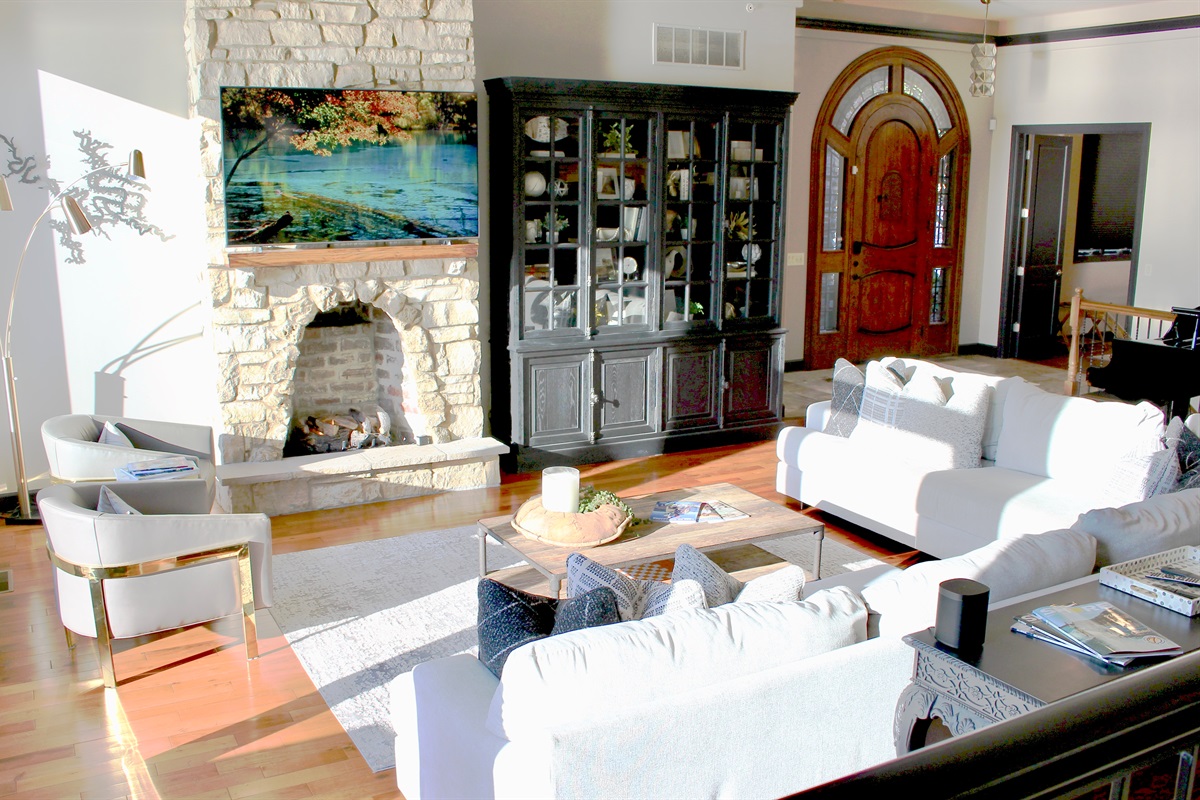 Great room with plenty of seating, grand piano, fireplace, and magnificent views of the lake.