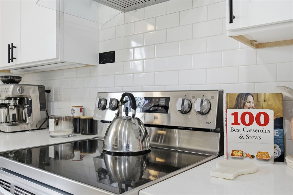 Electric stovetop and oven with kettle, backsplash tile, and modern cooking setup.