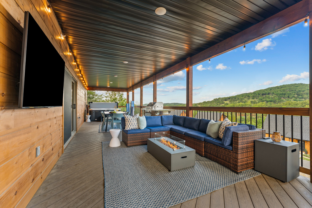 Relax on the spacious covered deck with a sectional, gas fire table, hot tub, and sweeping Ozark hill views near Branson.