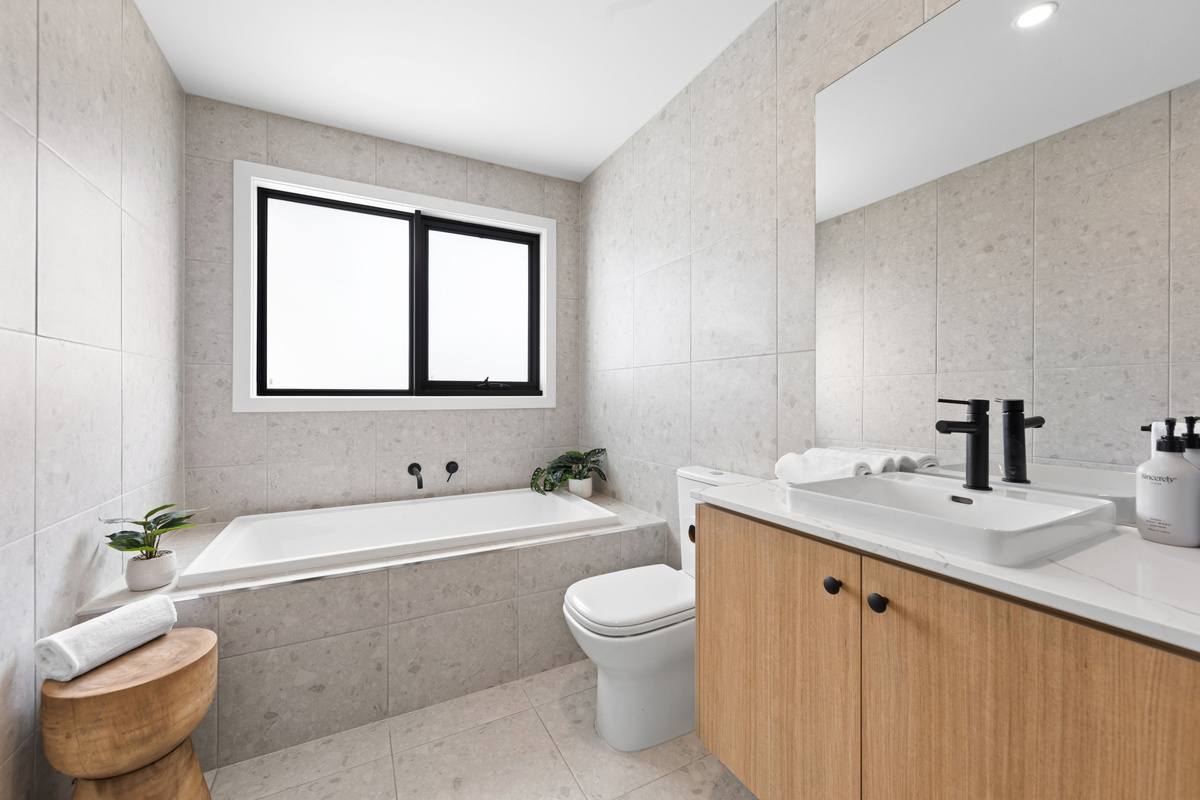 Main bathroom with a bath under the window, toilet, and a timber vanity with basin and black tapware.