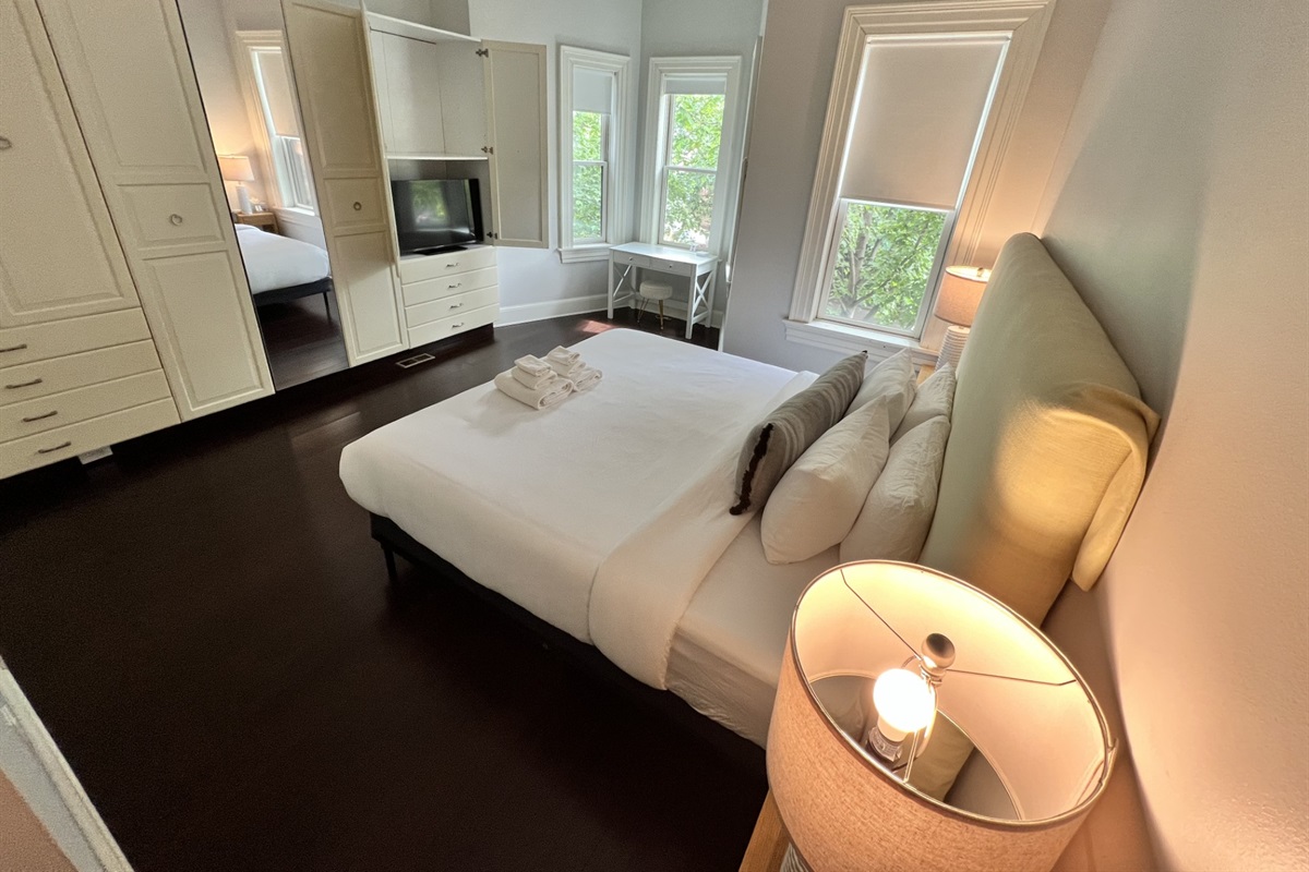 Spacious main bedroom with a newly upgraded plush Serta king bed, tranquil tree-lined views, a 40" Samsung 4K Smart TV, and a bright corner desk—ideal for work or planning your day in DC.