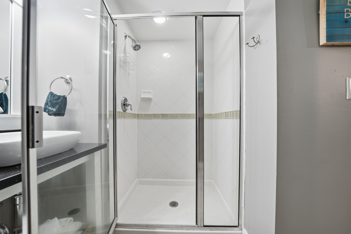 The shared full guest bath has modern vessel sinks tiled stand up glass shower.