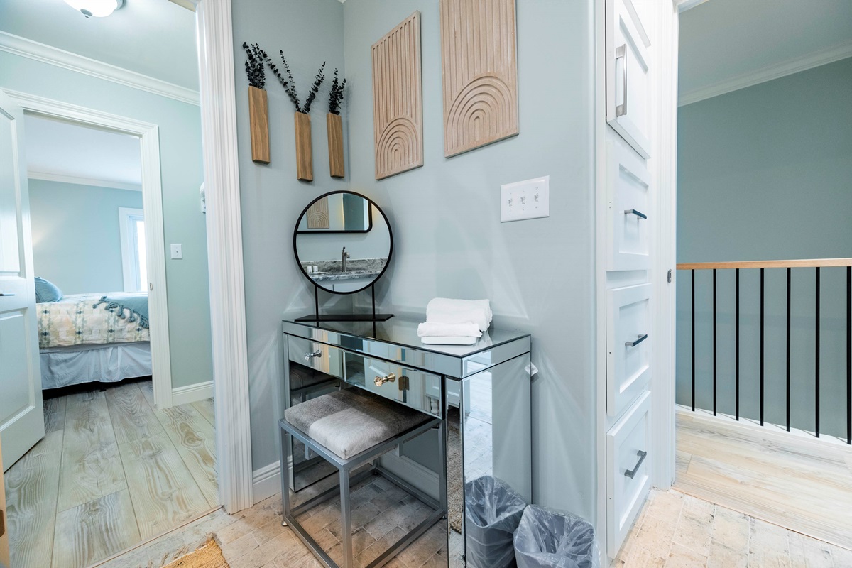 Charming vanity area with a mirrored desk, stool, wall art, and warm, cozy bedroom vibes.
