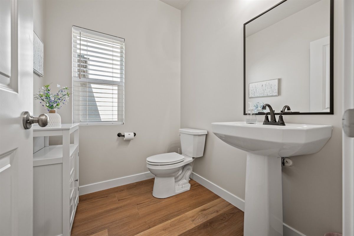 Charming and practical half bath on the main level with a pedestal sink, oversized mirror, and convenient storage for guest essentials.
