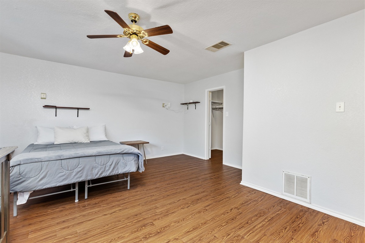 King Bedroom with ceiling fan, closet storage, hardwood floors, and comfortable gray bedding. Extra pillows and blankets provided. Ideal for extended stays and military visits near Randolph AFB and Fort Sam Houston.