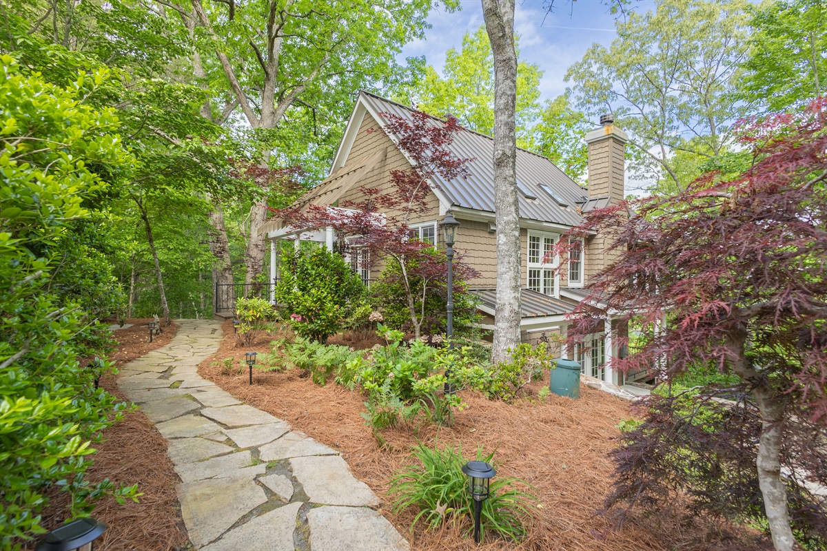 A charming stone walkway welcomes you to the home, surrounded by beautifully landscaped grounds and peaceful wooded scenery.