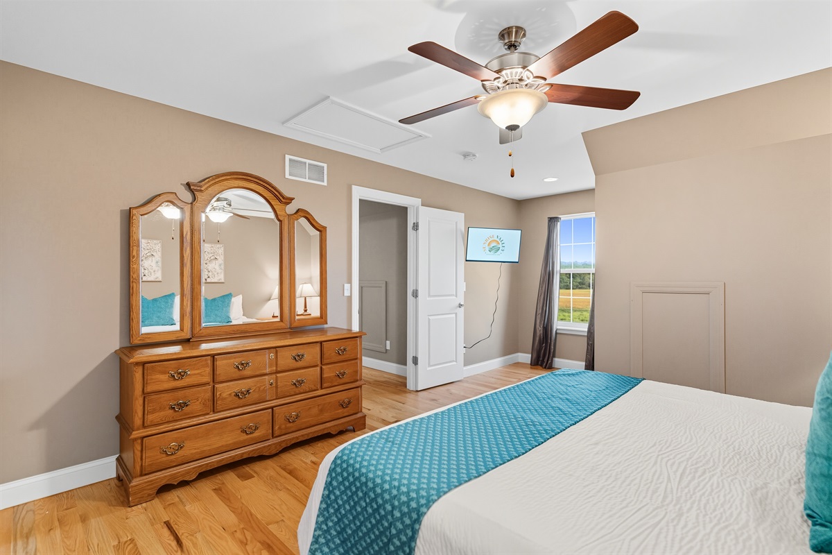 Spacious king bedroom with dresser and smart TV.