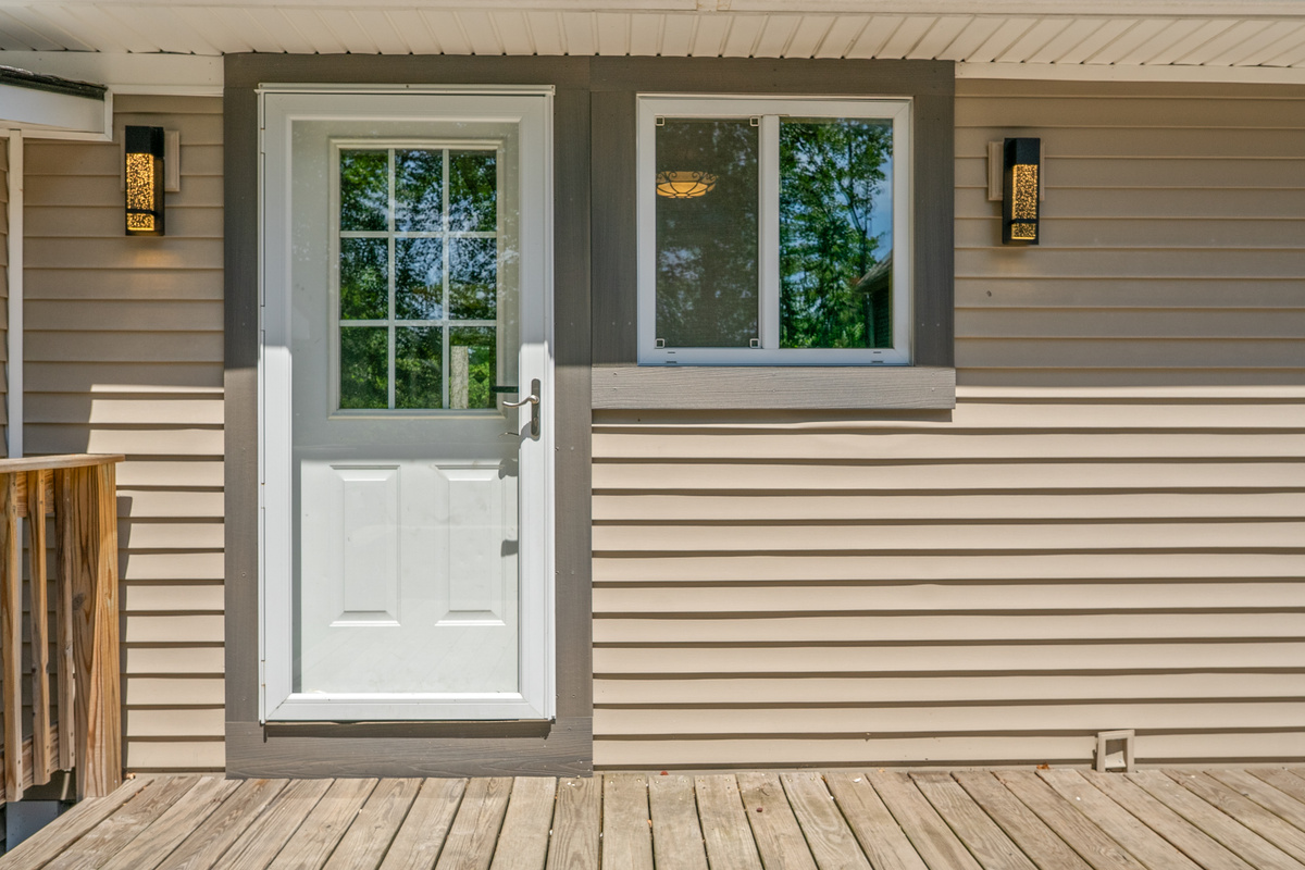 Open the glass-paneled entry door leading from the wooden deck straight into the home's interior. This flat, step-free threshold connects the outdoor living space directly into the eat-in kitchen area for seamless indoor-outdoor hosting.