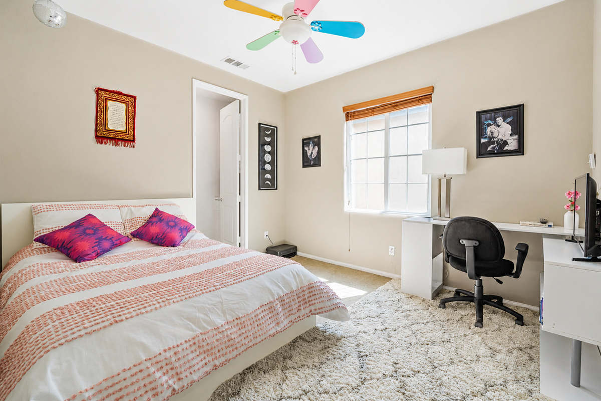 Bedroom with a comfortable bed, desk workspace, and a fun colorful ceiling fan.
