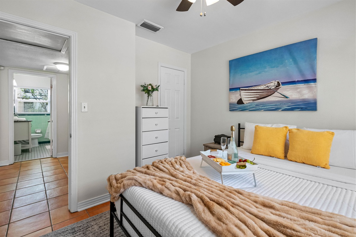 At the center of the room is a sleek, queen-size bed with a minimalist black metal frame and a supportive mattress dressed in crisp, hotel-quality linens.
