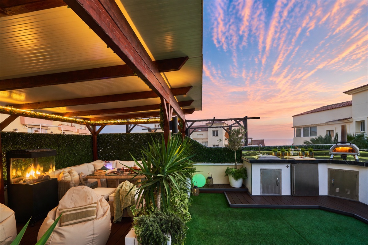 Fire up the built-in barbecue or the wood-fired pizza oven and enjoy cooking with a view. The fully equipped outdoor kitchen features a sink, fridge, and prep space with subtle lighting for evening meals. Dine under the open sky at the outdoor table, surro
