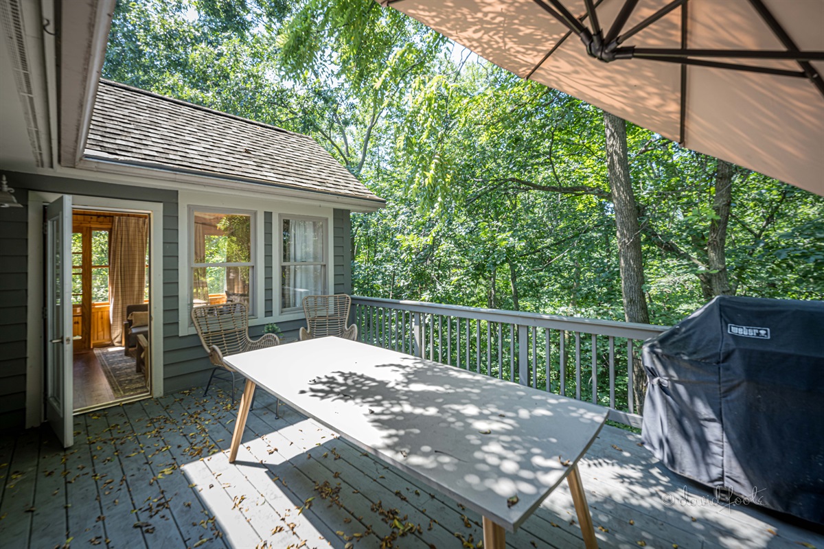 Deck overlooks woods and includes gas grill, table that accommodates 8 guests, and lounge chairs for two