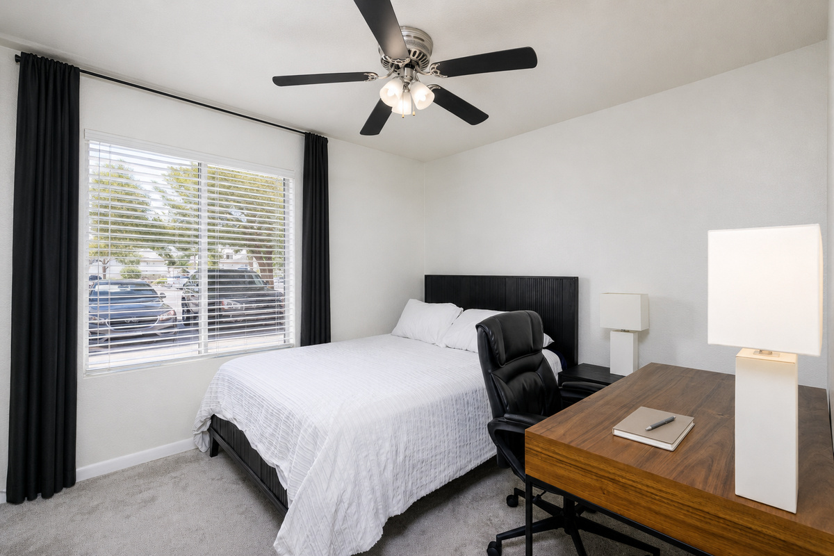 Bedroom with queen bed, dedicated desk, ceiling fan, and natural light for work or rest.