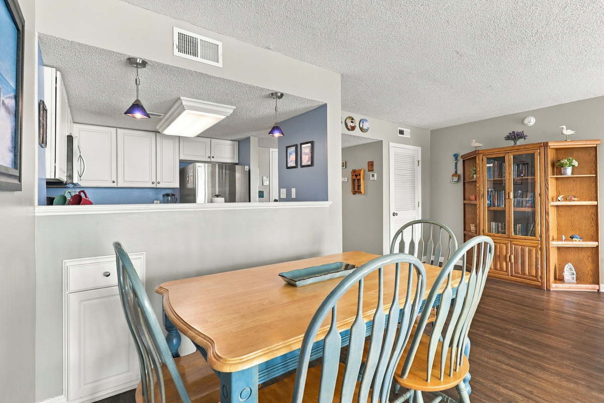 Dining area looking toward the kitchen, featuring a wooden table with blue chairs, a built-in hutch, and an open layout into the main living space.