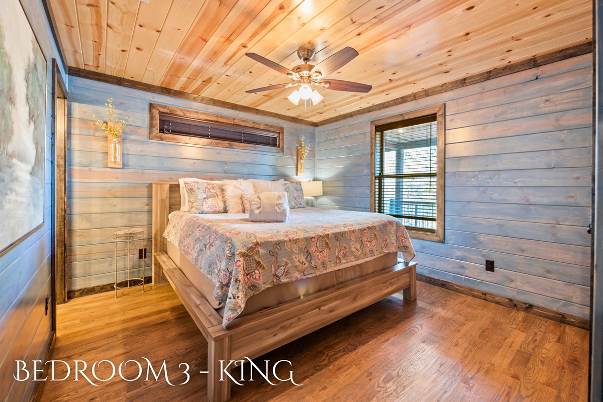 A welcoming bedroom with a king-sized bed, adorned with a floral patterned bedspread, set against a backdrop of warm wood paneling and natural light.