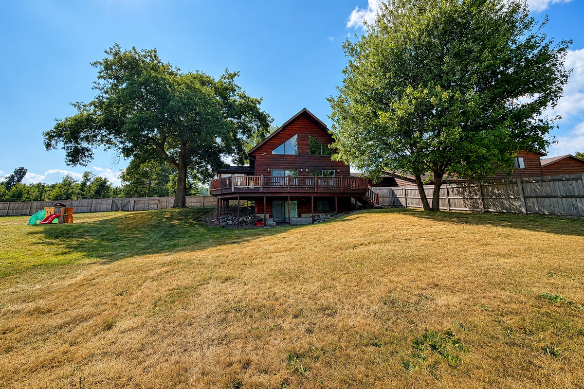 Wide exterior view shows the House surrounded by open lawn, mature trees and peaceful Wisconsin scenery.
