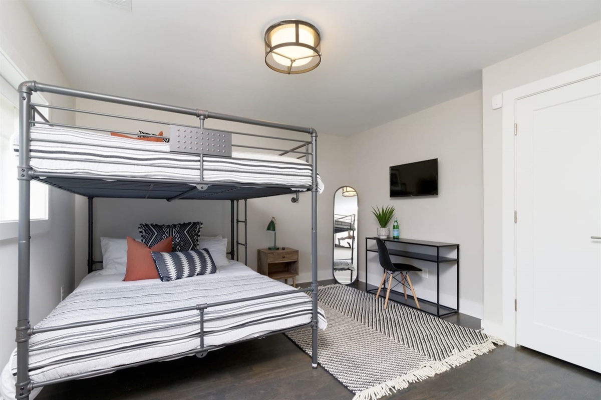 - Stylish bunk bed on bottom and twin up top, dressed in modern striped linens - Includes a sleek desk, wall mounted TV, and tall mirror for comfort and convenience - Monochrome rug and minimalist décor create a polished, cozy sleep and work space
