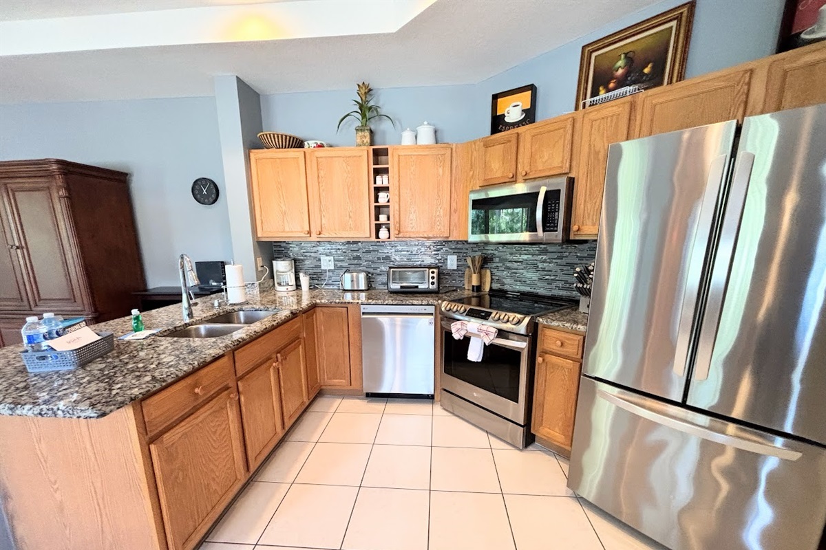 Fully equipped kitchen with stainless steel appliances, granite countertops, tile flooring, and plenty of cabinet space.