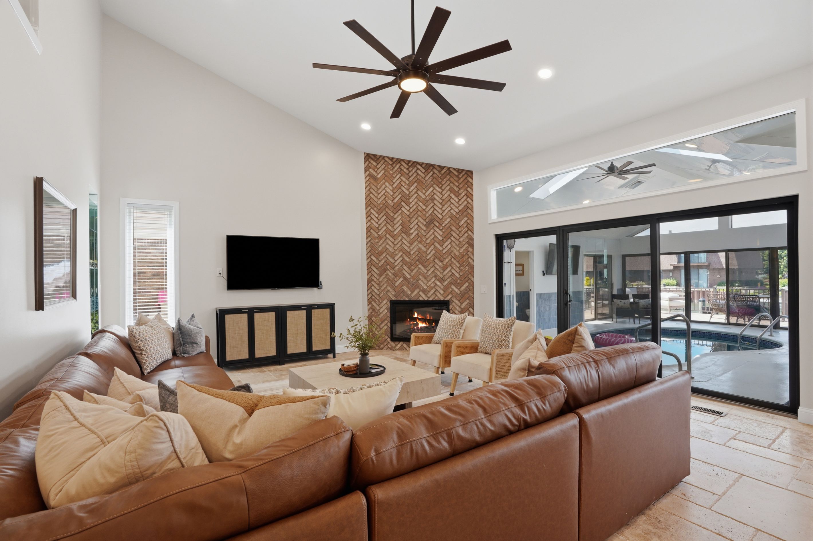 Gather in this spacious open-concept living room featuring a cozy sectional, modern fireplace, soaring ceilings, and seamless indoor-outdoor flow perfect for relaxing and entertaining.