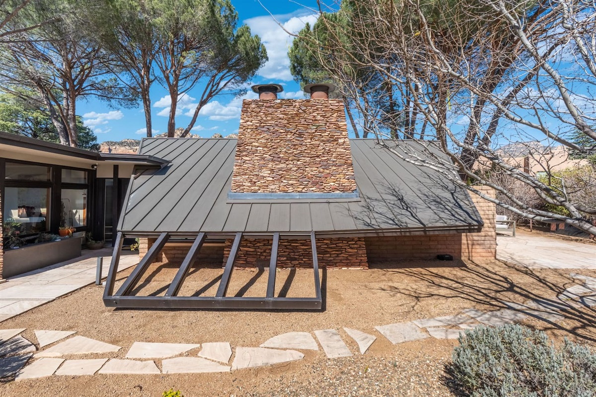 Distinctive stone chimney and sloped roofline framed by desert landscaping and mountain views.