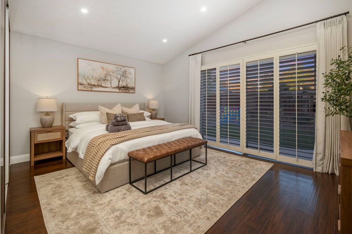 The primary bedroom showcases a king-size bed and sliding doors that open to the backyard, flooding the space with natural light. The seamless indoor-outdoor flow enhances the room’s airy, serene atmosphere, perfect for a relaxing retreat.