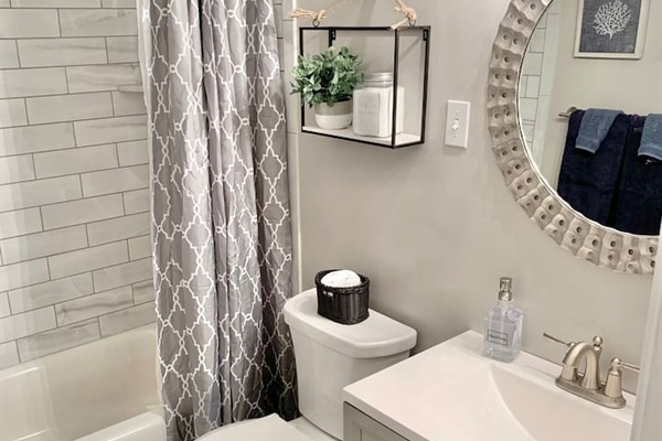 This modern full bath features a clean white vanity and a subway-tiled tub/shower combo. Coastal decor, like the round textured mirror and framed coral art, creates a bright, refreshing space for your daily routine.