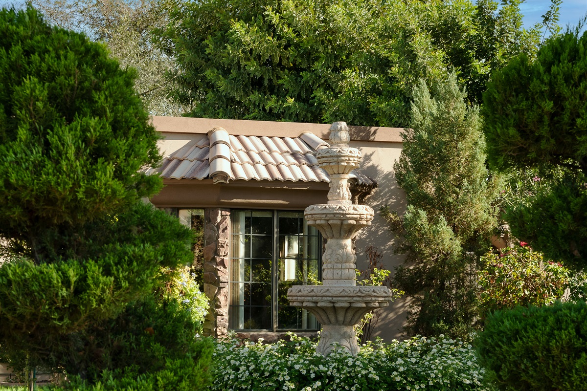 Unwind in this tranquil garden hideaway, where rich greenery and a charming stucco structure create a secluded outdoor sanctuary.