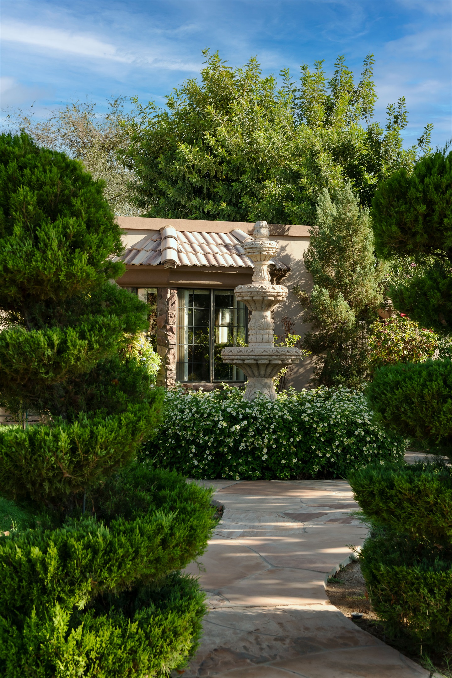Unwind in this tranquil garden hideaway, where rich greenery and a charming stucco structure create a secluded outdoor sanctuary.