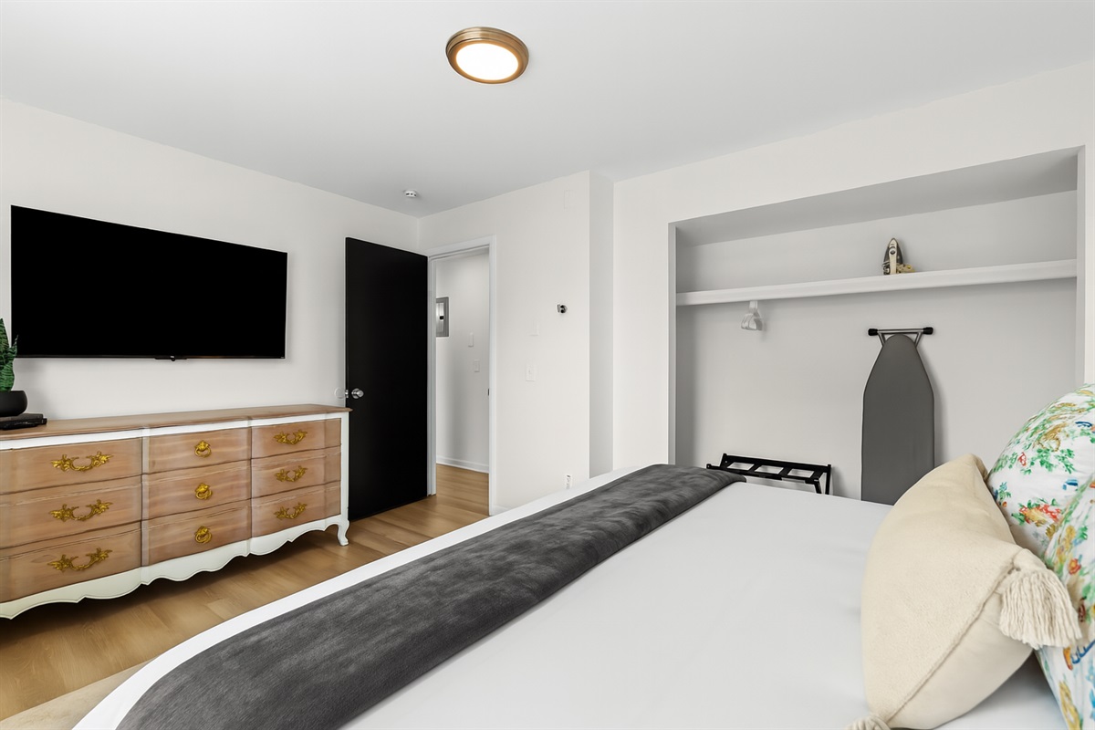 Spacious bedroom with a Smart TV, dresser storage, and cozy bedding for restful nights.