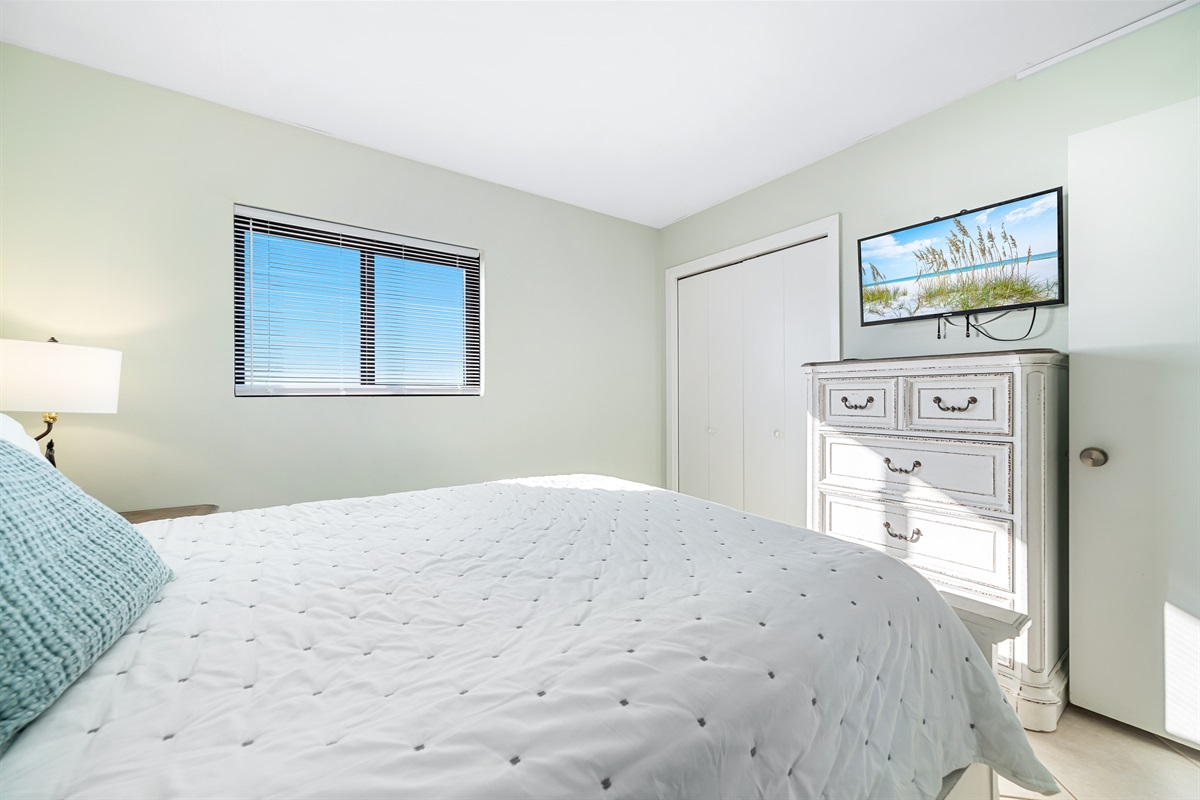 This well-appointed bedroom features a queen-size bed with a decorative headboard, crisp white bedding, matching nightstands with lamps, and tile flooring for easy maintenance.