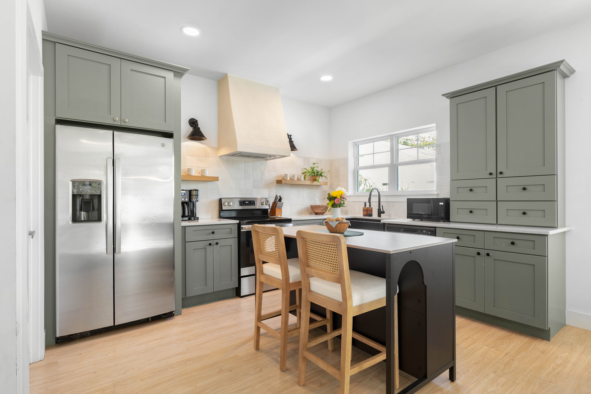 Everything a real cooking week needs: full-size fridge, electric range, a tall pantry and an island with room to spread out on. Two cane stools pull up for the ones who help mainly by watching closely.
