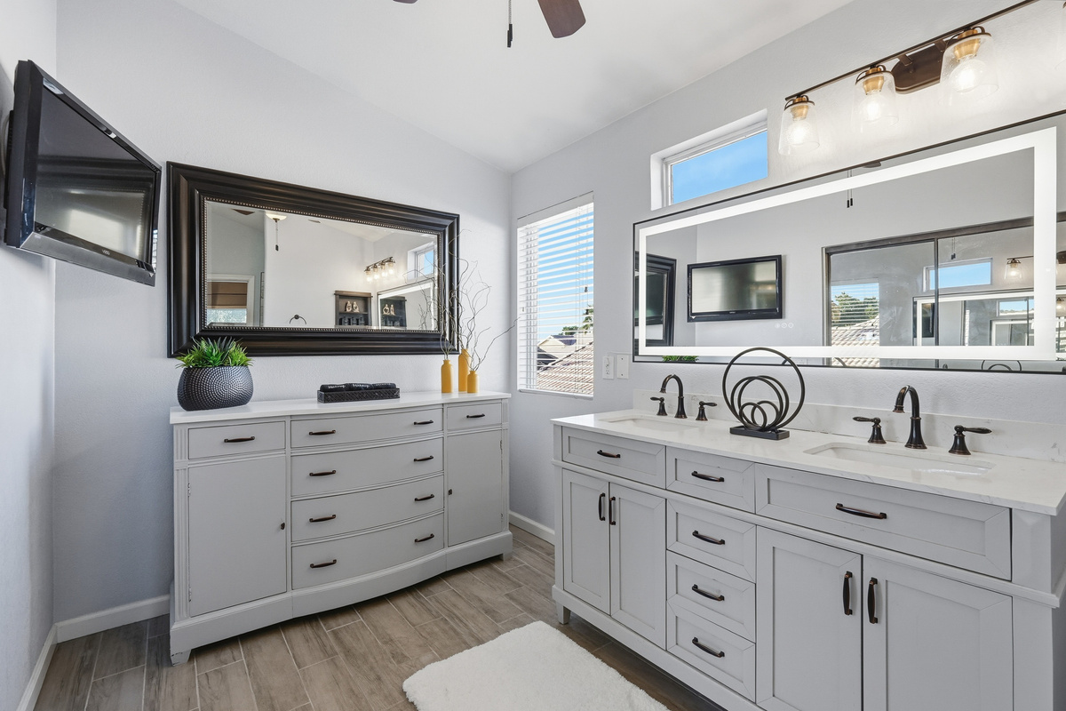Master BathroomMaster bathroom with double vanity, dresser storage, wall-mounted TV, bright mirror lighting, and plenty of space to get ready.