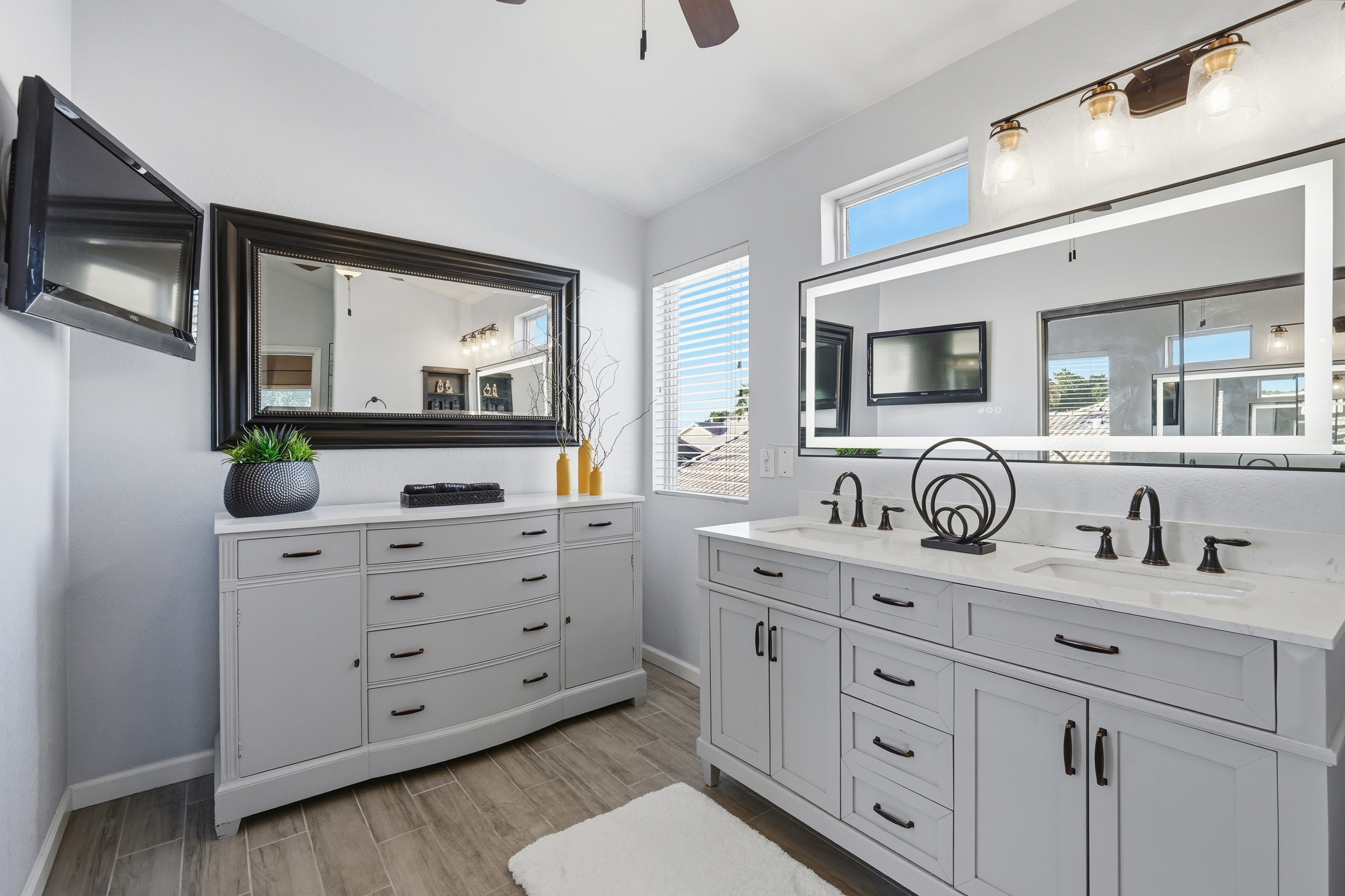 Master BathroomMaster bathroom with double vanity, dresser storage, wall-mounted TV, bright mirror lighting, and plenty of space to get ready.