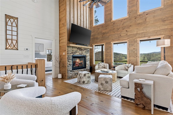 Spacious and inviting with window filled wood-paneled walls, stone fireplace, and breathtaking pasture views. Plenty of cozy seating—plush sofas, curved bouclé chairs, and ottomans—perfect for large family gatherings and relaxing together.