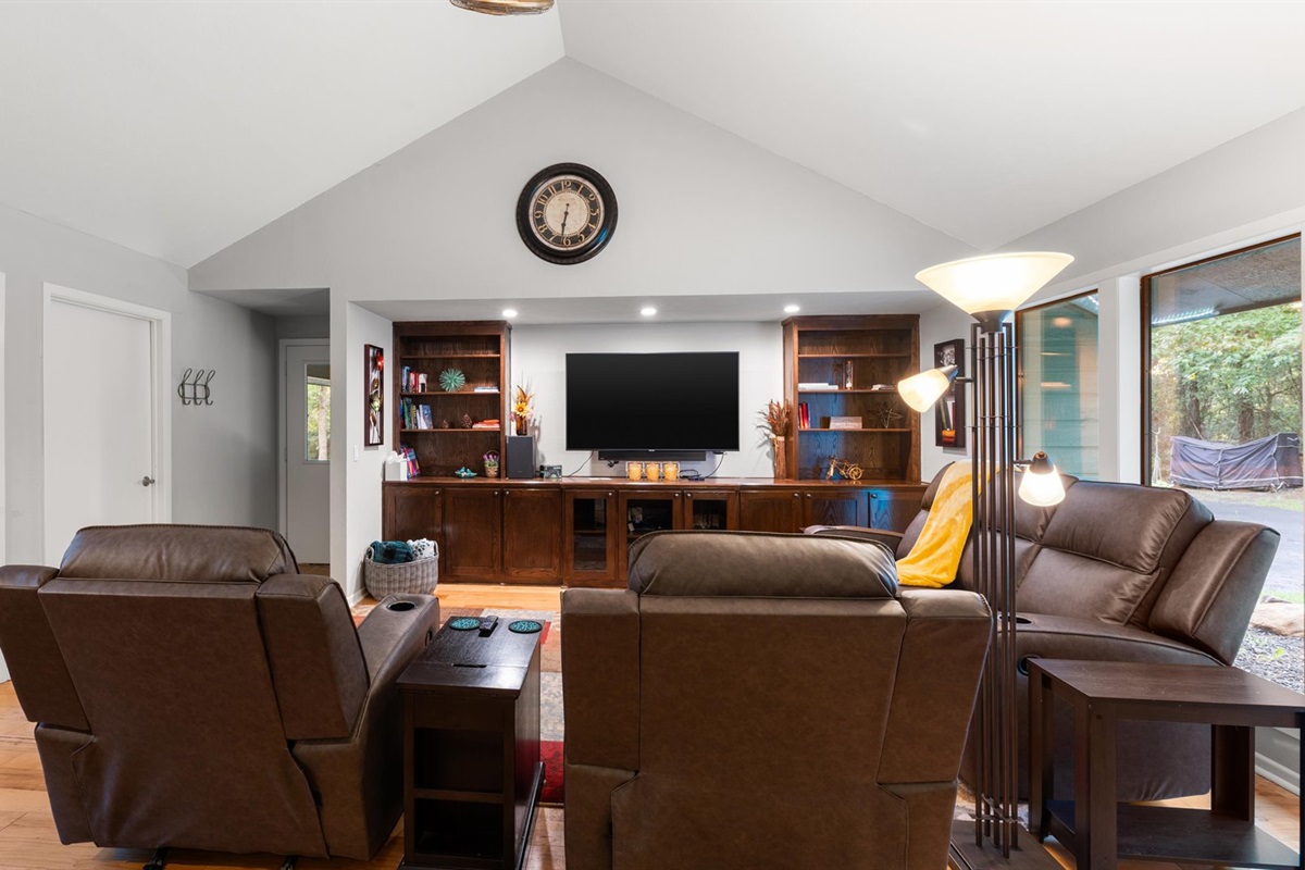 Living room features a reclining couch, recliners, a bistro table, and a wet bar with a refrigerator and ice maker. A 65" TV and plenty of cozy throws make it perfect for relaxing.