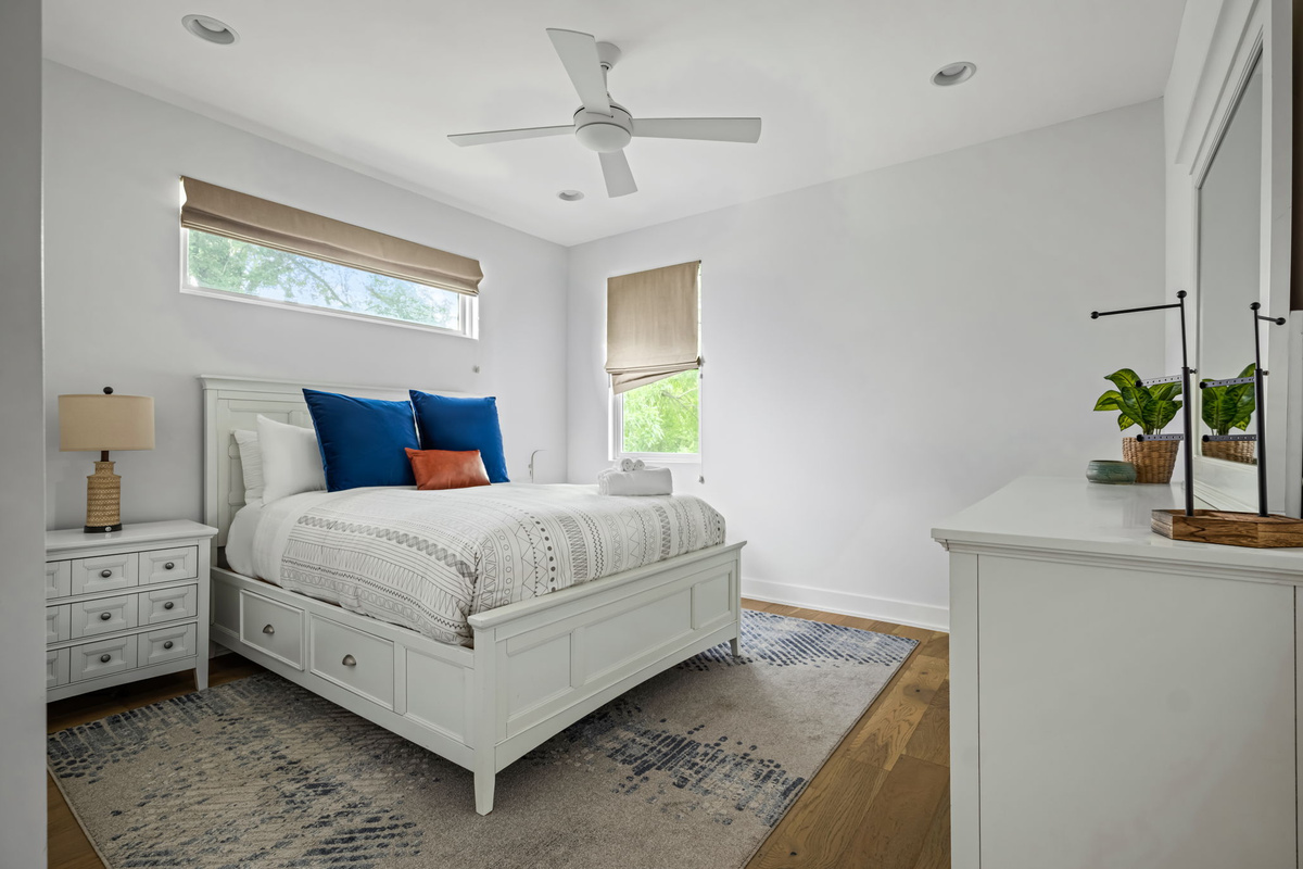 Charming guest bedroom with a plush white bed, ceiling fan, and large windows bringing in plenty of natural light.