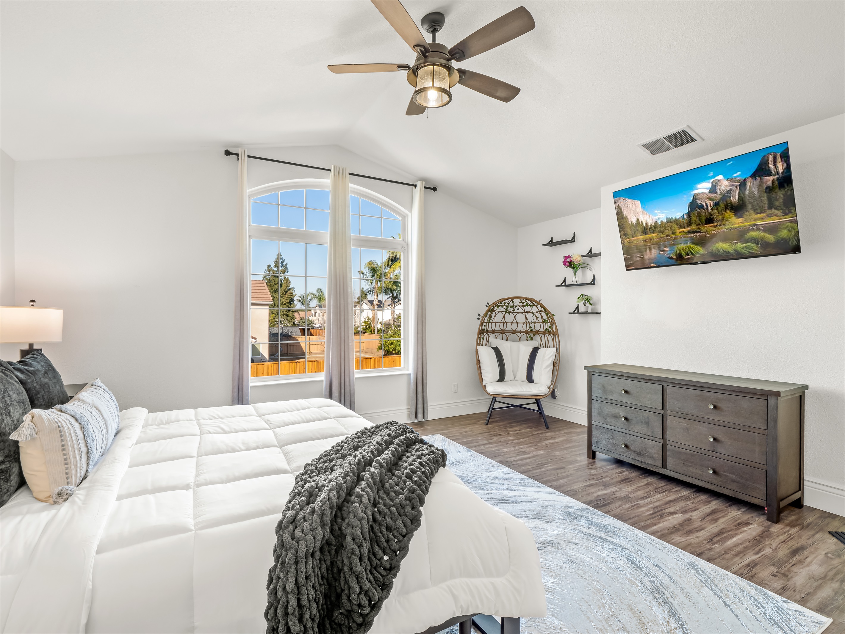 Elegant primary retreat featuring dramatic vaulted ceilings, a statement window, stylish seating nook, and in-room TV—luxury, light, and comfort all in one.