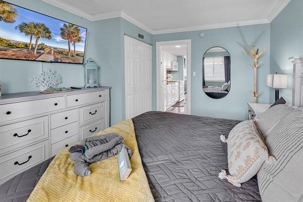 King bedroom with wall-mounted flat-screen TV, dresser, and soft coastal tones throughout