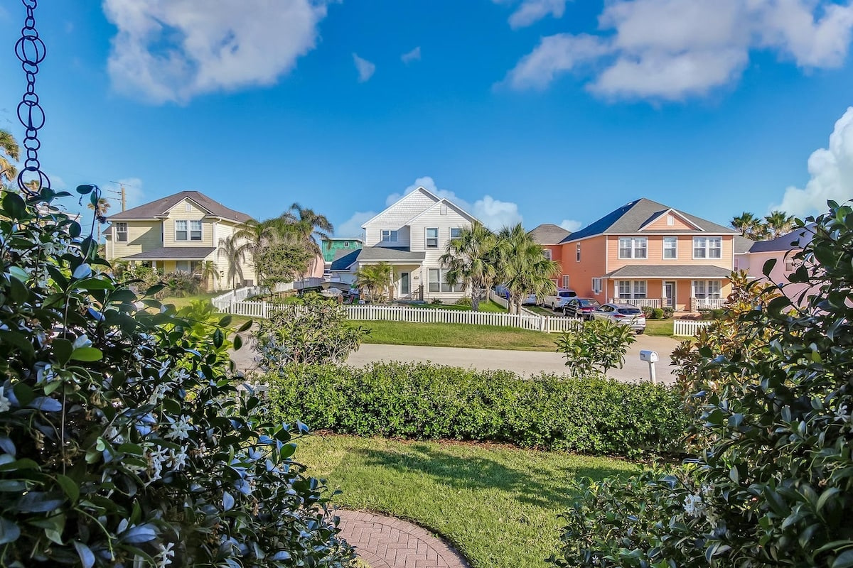 A quiet residential street of low beach houses and mature palms, a few blocks back from the water. There are neighbours on every side here, which is why the ten till eight quiet hours genuinely do matter.