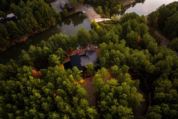 An aerial view of The Cove, beautifully surrounded by a dense forest and a peaceful lake. This secluded getaway offers privacy while still being close to Hochatown and local attractions.