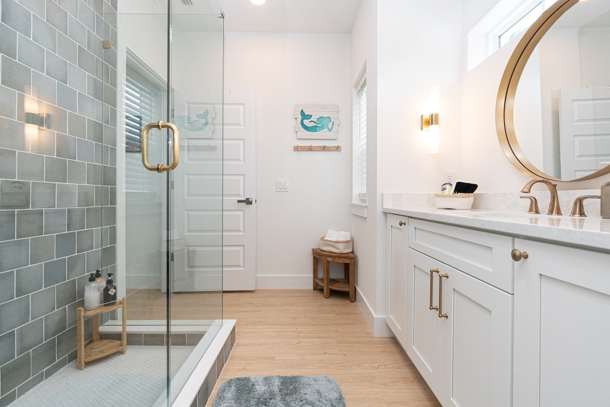 Sea-glass tile, a glass walk-in shower, and a wide vanity with room for two people's things at once. Small mercies after a long beach day: plenty of hot water, good light, and somewhere to set the sunscreen down.