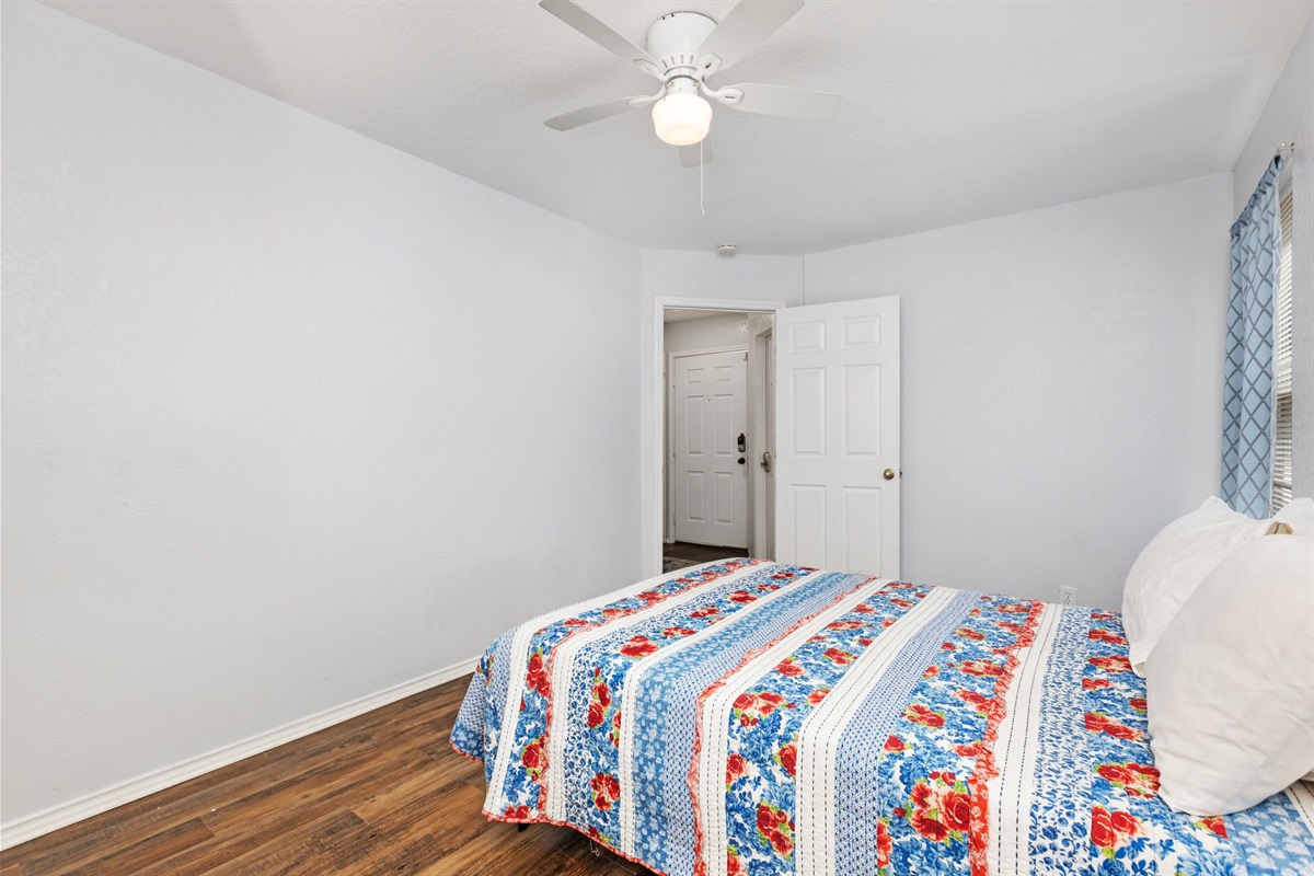 Spacious queen bedroom with colorful bedding, ceiling fan, closet storage, and hardwood floors. Hotel-quality cotton linens, extra pillows, and blankets provided. Current decorative blankets, bedding, and wall art are not shown in these photos.