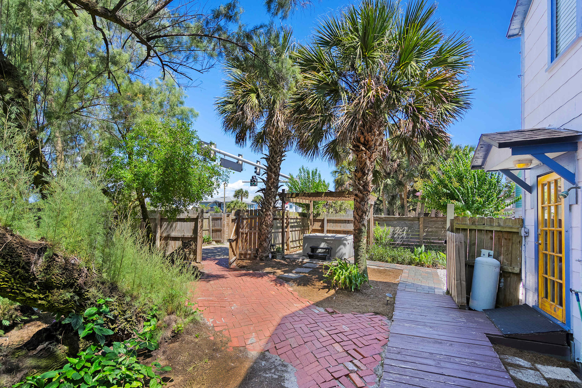 The brick path runs down the side of the house past the palms, linking the parking, the courtyard and the stairs up to your door. Everything on this little property sits a few easy steps from everything else.