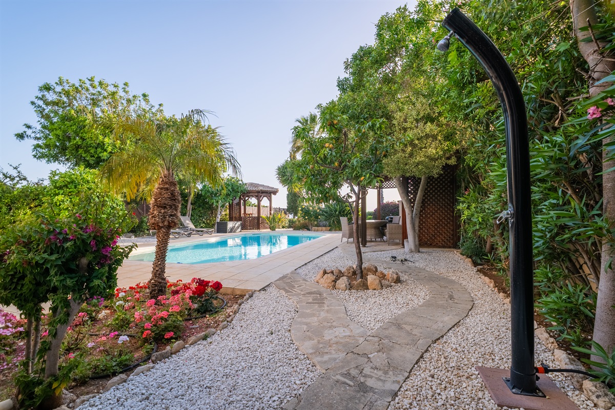 The pool is surrounded by a lush garden with fruit trees, palm trees, and flowers.